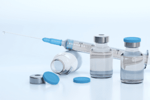 Glass vials with clear liquid and a syringe with a drop of clear liquid on the end.